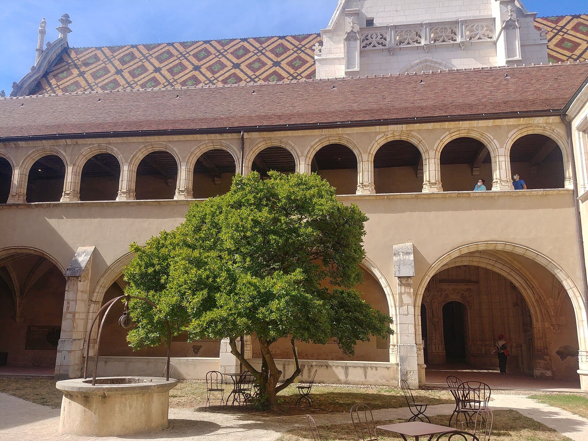 Le grand cloître du monastère de Brou : galeries à arcades en pierre claire autour d’un arbre et d’un puits.