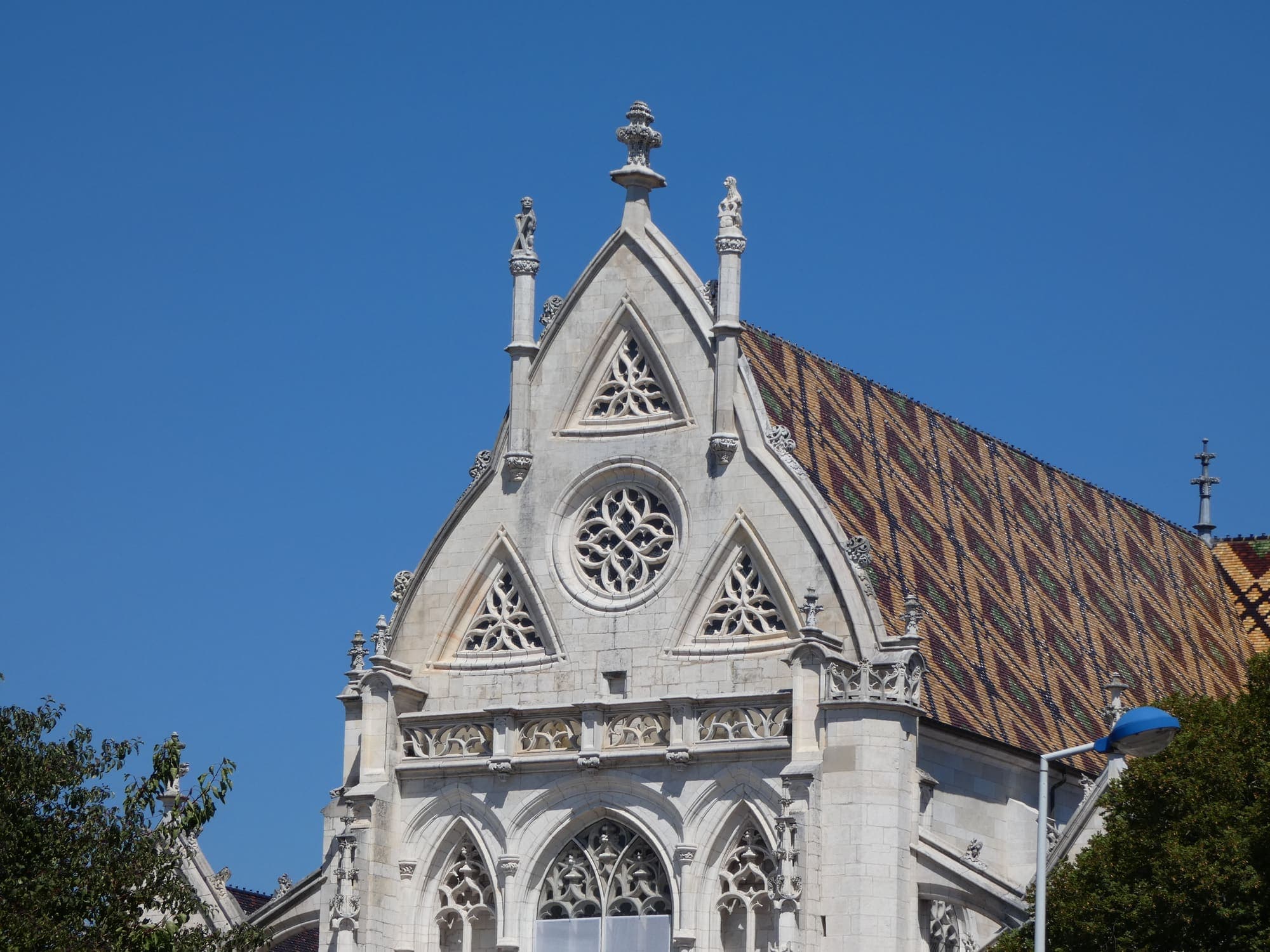 Le pignon de l’église de Brou, en pierre blanche sculptée, et sa toiture de tuiles vernissées en losanges, sous un ciel bleu.